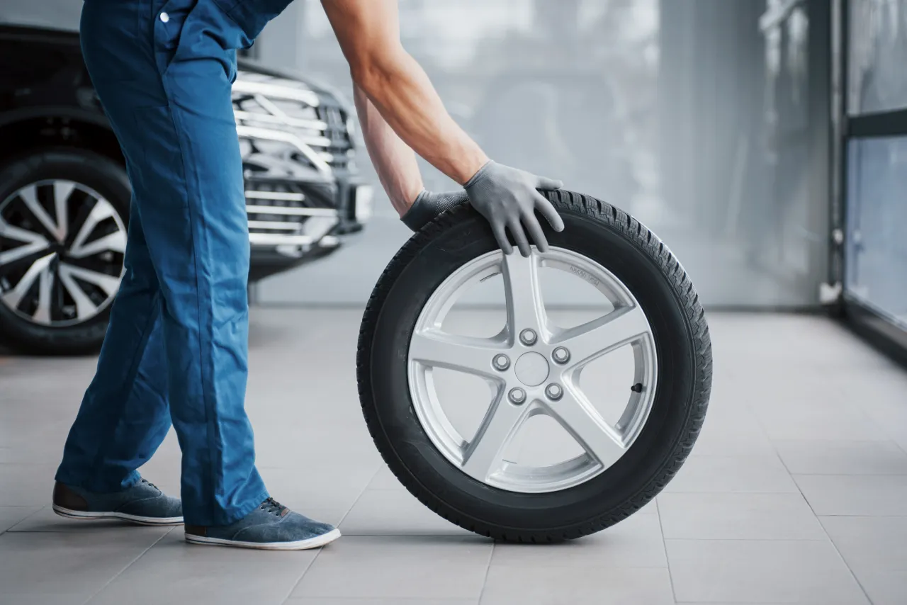 Mechanic holding a new car tyre next to a car 